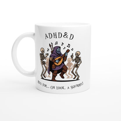 A white mug displays a cartoon illustration of a D&D bard playing music for dancing skeletons, accompanied by the words "ADHD & D" and "Roll For... Oh Look, A Squirrel!