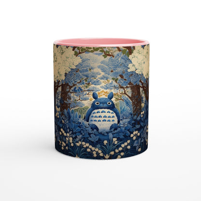 A ceramic mug depicts Totoro from Studio Ghibli sitting within a blue and pink chinoiserie-style cherry blossom forest scene.