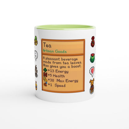 A white mug displays a Stardew Drinks pattern featuring pixelated sprites and a description of tea as an artisan good with energy and health boosts.