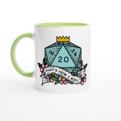 A white mug with a green handle and rim features an illustration of a D&D d20 die displaying "20" surrounded by floral elements and the phrase "That's How I Roll.