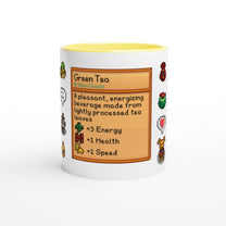 A white mug features a Stardew Drinks pattern depicting a green tea beverage card with pixelated sprites and information about its effects.