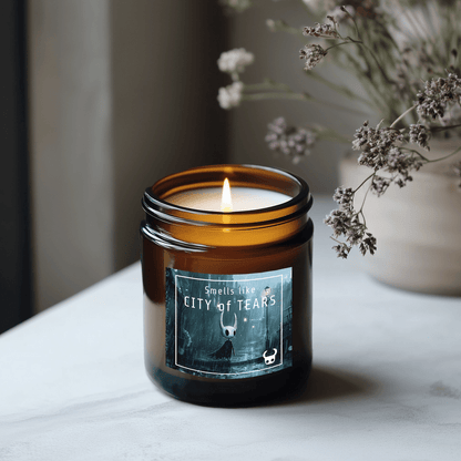 A lit amber glass candle labeled "Smells like CITY of TEARS" features artwork inspired by the video game Hollow Knight.