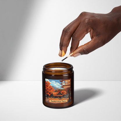 A hand holds a wooden match as it is lowered into a Stardew Valley scented candle featuring an illustration of Featherstone Farm on its label.