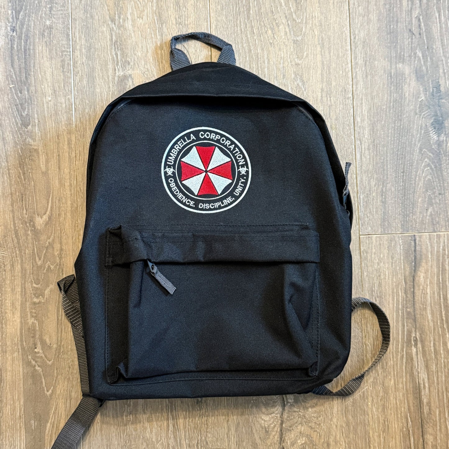 Black backpack with Umbrella Corporation logo on a wooden floor