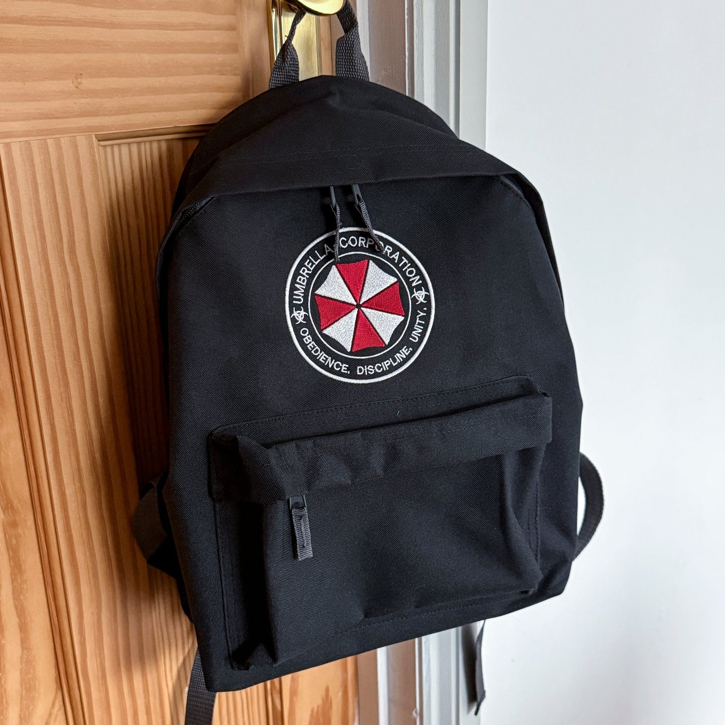 Black backpack with Umbrella Corporation logo hanging on a door