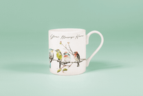 A white china mug displays watercolour birds perched on a branch alongside handwritten text reading "Your Message Here.