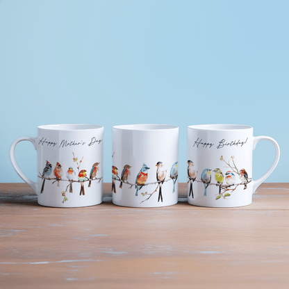 Three white china mugs display watercolour illustrations of birds perched on a branch, with "Happy Mother's Day" and "Happy Birthday" printed on two of them.