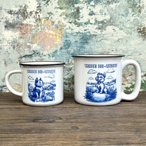 The Quirkify Stardew Valley Chinoiserie Campfire Mug is a blue and white toile ceramic cup featuring house, tree, and mountain artwork with "Stardew Valley" printed on it, displayed on a wooden surface against a multicolored wall.