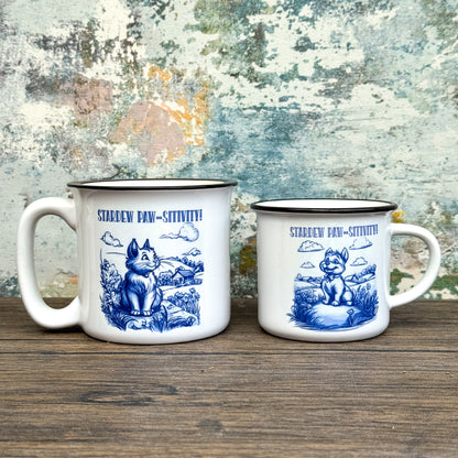 The Quirkify Stardew Valley Chinoiserie Campfire Mug is a blue and white toile ceramic cup featuring house, tree, and mountain artwork with "Stardew Valley" printed on it, displayed on a wooden surface against a multicolored wall.