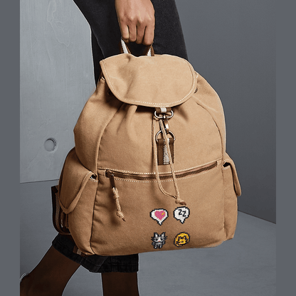 A tan canvas bag resembling a Stardew Valley backpack features pixelated designs of a cat, heart emote, and other icons.