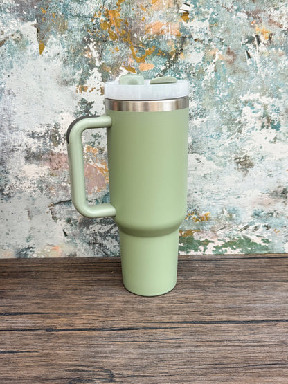 A green Witchy Boho engraved tumbler with a handle and lid sits on a wooden surface against a textured background.