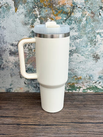 A white Witchy Boho engraved tumbler with a handle and lid sits on a wooden surface against an abstract blue and brown textured background.