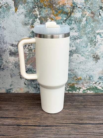A white Witchy Boho engraved tumbler with a handle and lid sits on a wooden surface against an abstract blue and brown textured background.