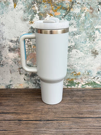 A white Witchy Boho engraved tumbler with a handle and lid sits on a wooden surface against an abstract textured background.