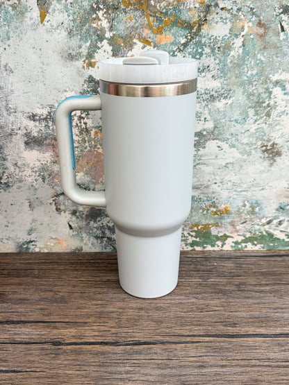 A white Witchy Boho engraved tumbler with a handle and lid sits on a wooden surface against an abstract textured background.