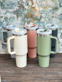 Six 40oz tumblers in various colors are lined up on a wooden surface, likely representing the Octopus Engraved tumbler collection inspired by D&D and Cthulu.
