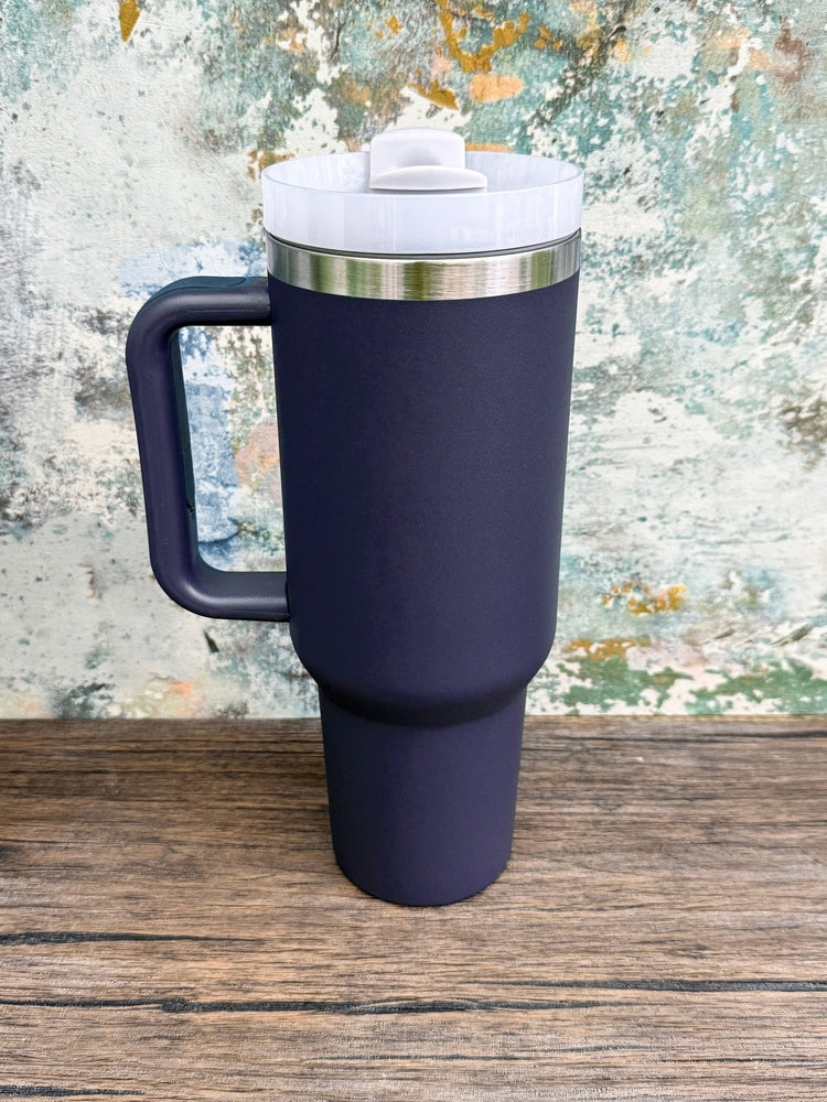 A dark blue Witchy Boho engraved tumbler with a handle and lid sits on a wooden surface against a textured wall.