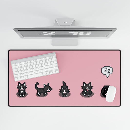 An extra large desk mat features a black and white pixelated pattern of tuxedo cats reminiscent of the computer game Stardew Valley, set against a pink background with a keyboard and mouse.