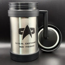 A silver travel mug resembling a thermos features the Star Trek delta shield logo and "U.S.S. Defiant NX 74205" printed on its surface
