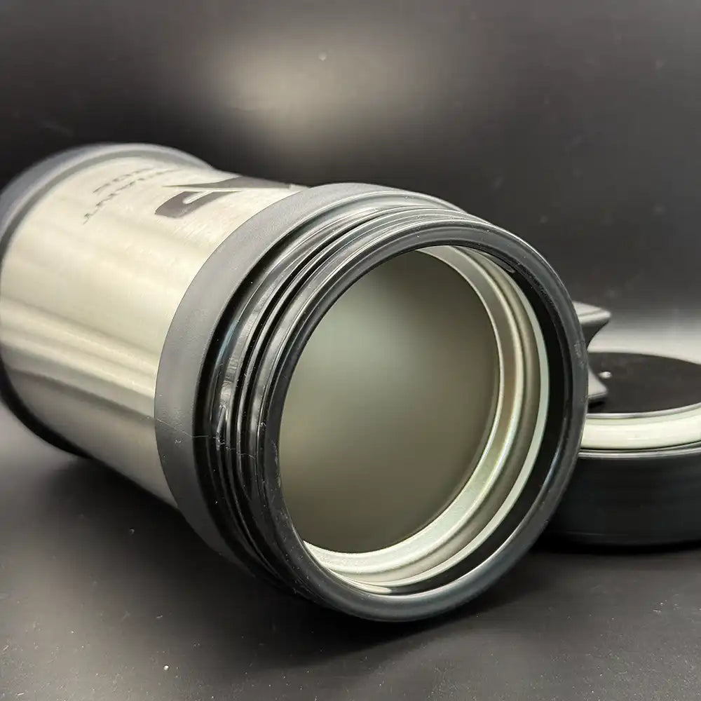 A silver travel mug resembling a thermos features the Star Trek delta shield logo and "U.S.S. Defiant NX 74205" printed on its surface