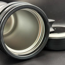 A close up of silver travel mug resembling a thermos features the Star Trek delta shield logo and "U.S.S. Defiant NX 74205" printed on its surface