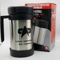 A silver travel mug resembling a thermos features the Star Trek delta shield logo and "U.S.S. Defiant NX 74205" printed on its surface, with original box