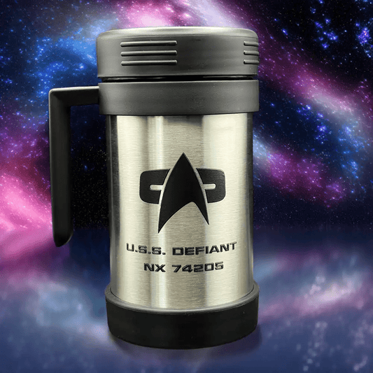 A silver travel mug resembling a thermos features the Star Trek delta shield logo and "U.S.S. Defiant NX 74205" printed on its surface against a backdrop of stars and nebulae.