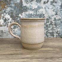 A handmade ceramic tea infuser mug with a lid sits on a wooden surface against a textured blue and white background.