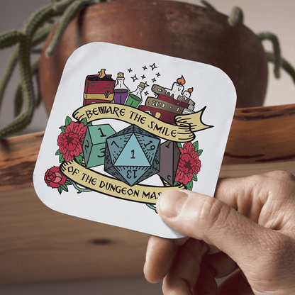 Sticker with dice design and text held by a hand, with a wooden surface and plant in the background