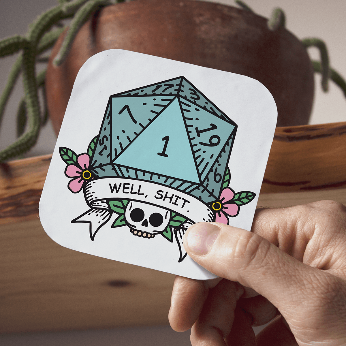 Coaster with a DnDn D20 die design and text held by a hand, with a plant in the background