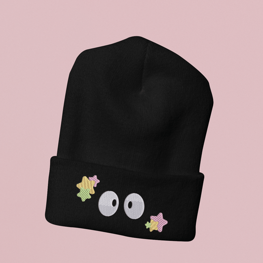 Black beanie hat on pink background with Ghibli inspired embroidery design of soot sprite eyes and stars on turned up cuff.