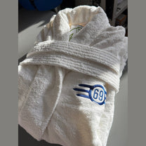 A white terry cloth bathrobe featuring a blue embroidered Fallout Vault-Tec logo on the chest.