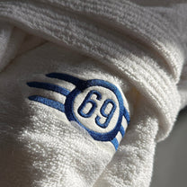 Close-up of a white terry cloth bathrobe featuring a blue embroidered Fallout Vault-Tec style logo with the number 69.