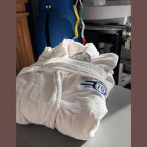 A folded white bathrobe featuring the blue and yellow Fallout Vault-Tec logo and number 76.