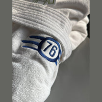 Close-up of a white terry cloth bathrobe featuring an embroidered blue Vault-Tec logo with the number 76 from the Fallout video game series.