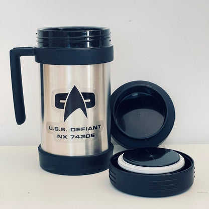 A silver Star Trek-inspired travel mug labeled "U.S.S. Defiant NX 74205" sits next to its black lid, both against a white background.
