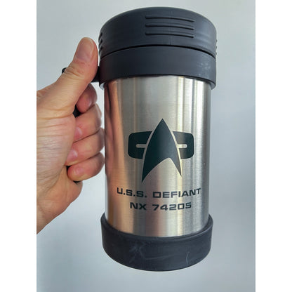 A hand holds a silver travel mug featuring the Star Trek delta shield logo and "U.S.S. Defiant NX 74205" printed on its surface.