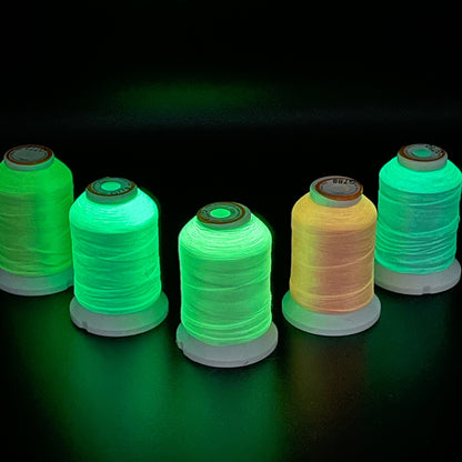 Six spools of glow-in-the-dark embroidery thread are arranged on a dark surface.