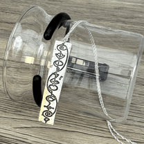 A sterling silver Vulcan IDIC calligraphy etched pendant hangs from a delicate chain, displayed against a clear glass container on a wooden surface.