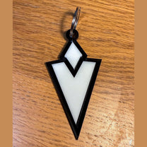 A 3D acrylic keyring featuring a white Skyrim inspired Quest Marker icon with a black border on a wooden surface.