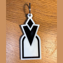A 3D acrylic keyring featuring a white and black Skyrim inspired Quest Marker icon on a wooden surface.