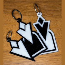 Two 3D acrylic keyrings featuring a black and white Skyrim inspired Quest Marker icon resting on a wooden surface.
