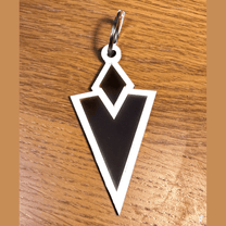 A 3D acrylic keyring featuring a black and white Skyrim inspired Quest Marker icon resting on a wooden surface.