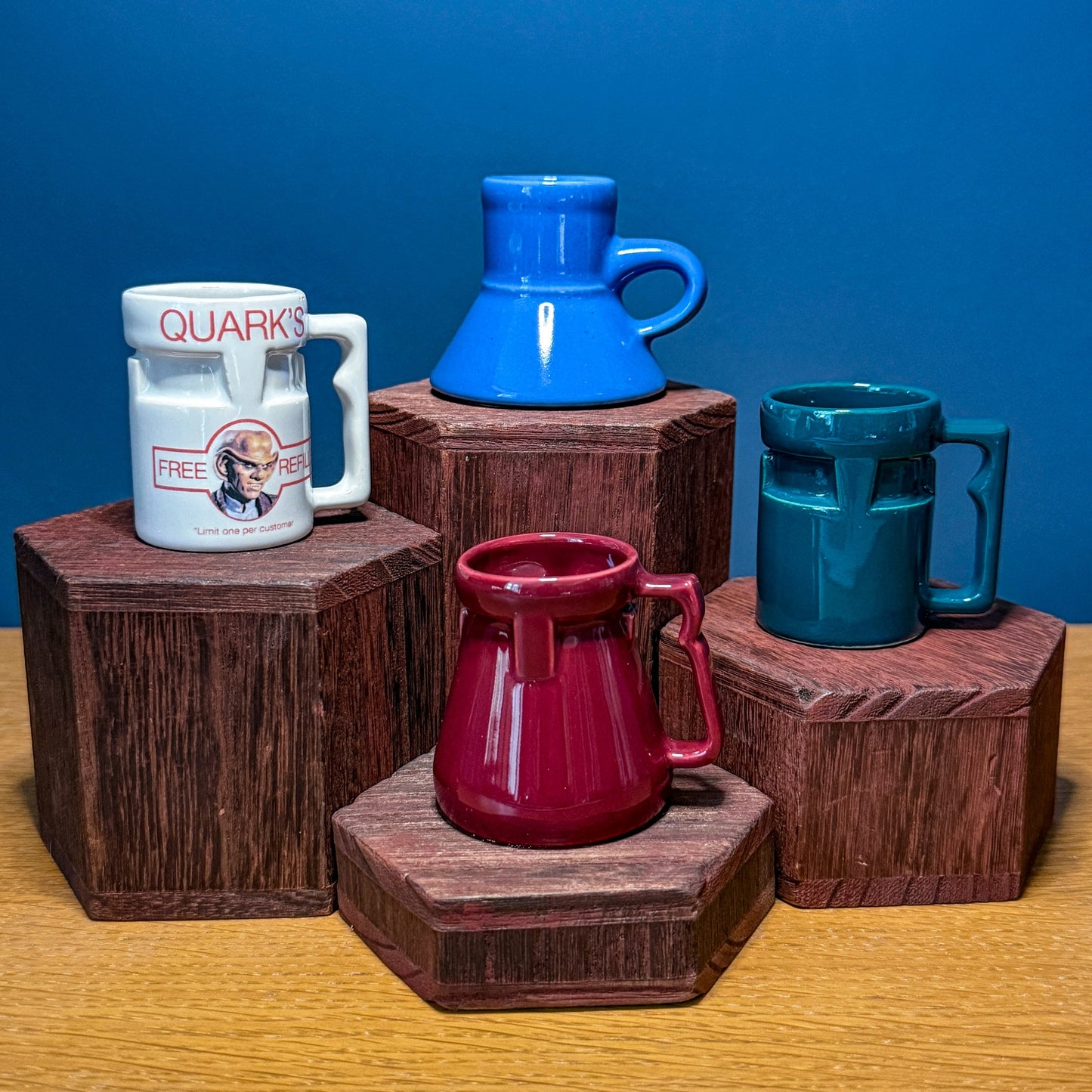 Four colorful Raktajino mugs on wooden stands against a blue background