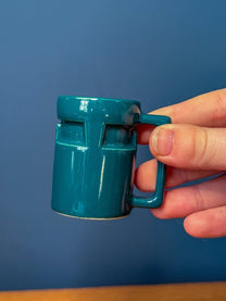 A person holds a small teal ceramic DS9 Mini Raktajino mug designed for espresso or shots.