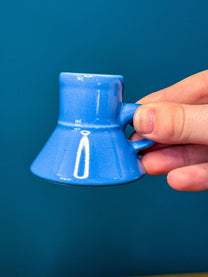 A person holds a small blue ceramic DS9 Mini Raktajino Mug designed for espresso or shots.
