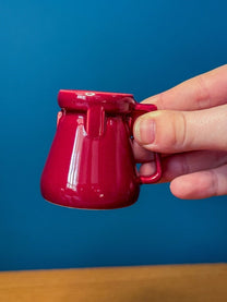 A hand holds a small, glossy maroon DS9 Mini Raktajino mug designed for espresso or shots.