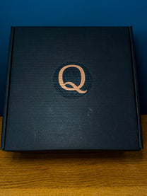 A black gift box for The DS9 Mini Raktajino Mug Set featuring a copper-colored letter Q on the lid.