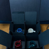 Four small colorful mugs for espresso or shots are displayed inside individual black compartments of a DS9 Mini Raktajino Mug Set box.