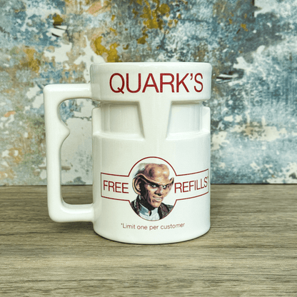 A white ceramic mug shaped like a beer stein displays "Quark's" and an image of Quark from Star Trek: Deep Space Nine advertising free refills.